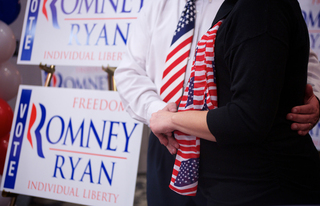 Mike and Yvette Bishoff embrace Yvette's pregnant stomach while posing for a photo next to Mitt Romney signage. 
